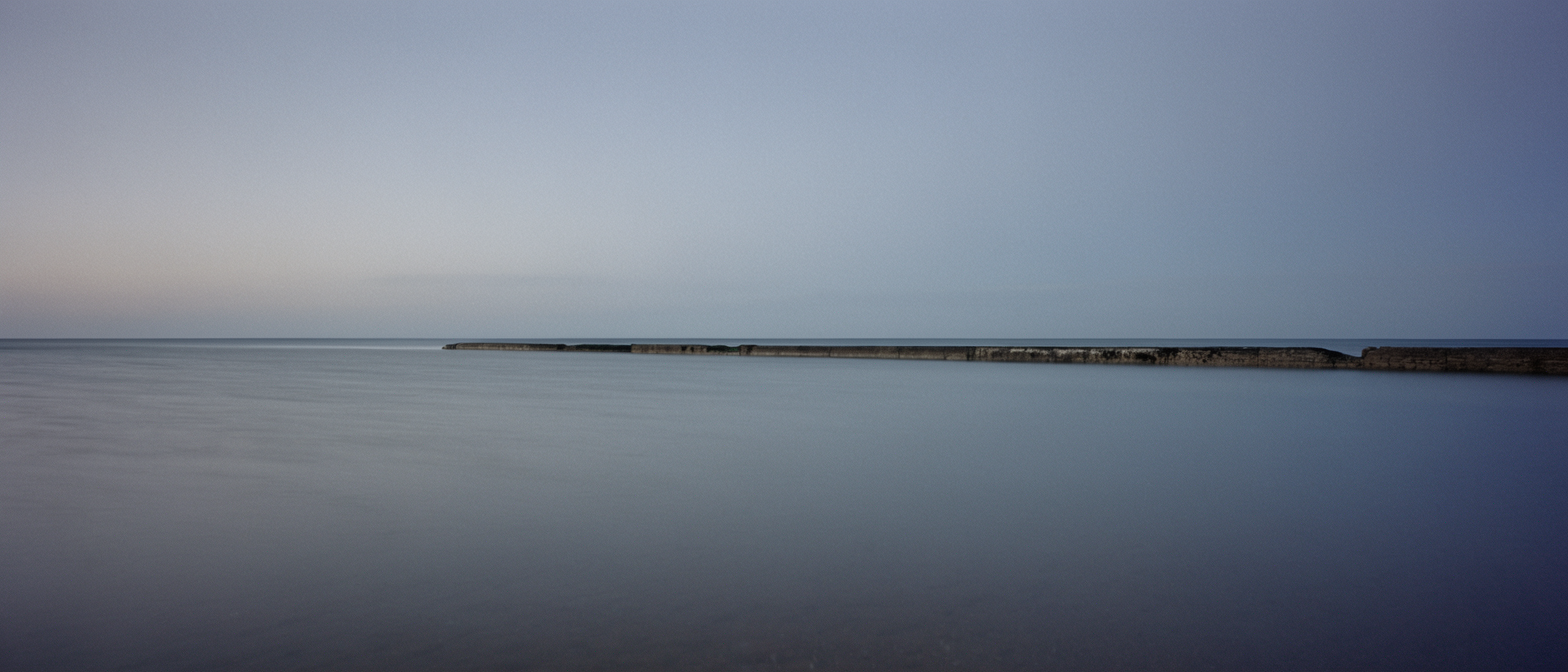 Flat tidal water meeting a pale horizon at blue hour